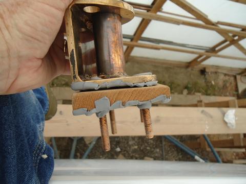 A good shot of the layers of butyl--under the bolts heads, between the base and the teak wedge, and between the teak and the deck. The holes on top of the teak