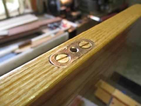 I made this small bronze inserts and mortised them in to the edge of the table. The center hole is tapped for a 10-24 machine screw that passes through the fidd